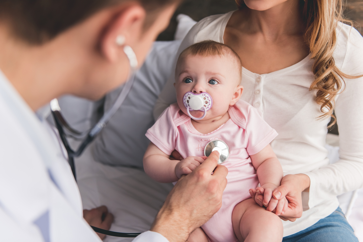 mamá sosteniendo a bebé mientras pediatra le diagnostica