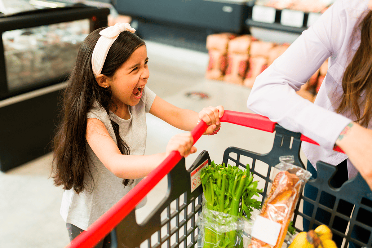 niña en el supermercado agarrada al carrito de las compras y gritando