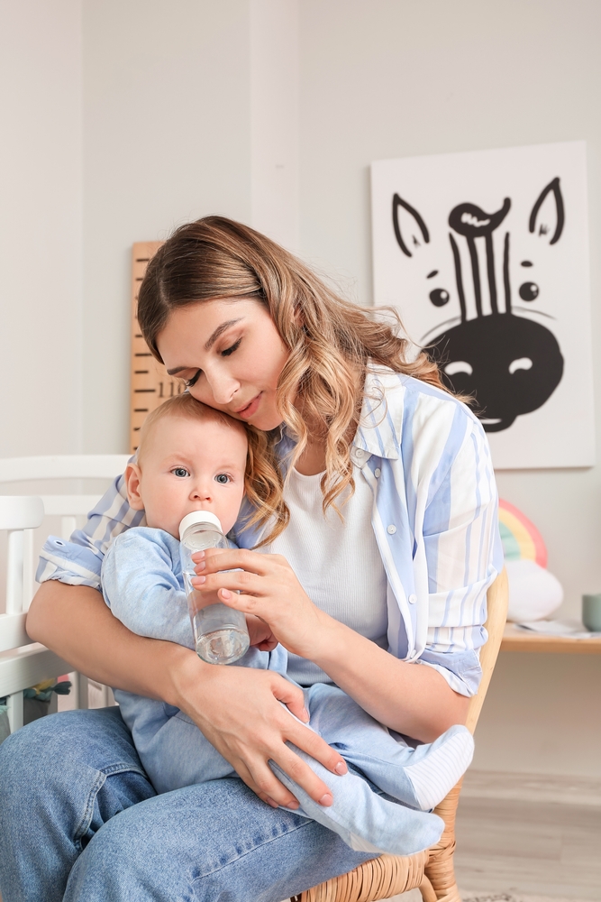 Young,Mother,Giving,Water,To,Her,Cute,Baby,At,Home