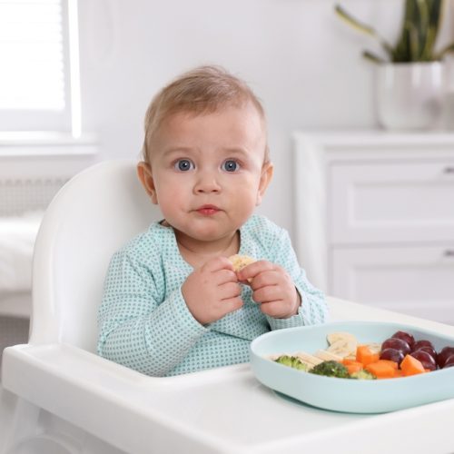 Cute,Little,Baby,Eating,Food,In,High,Chair,At,Home