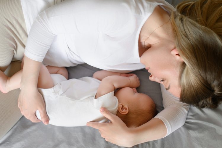 Mom,Lies,On,Bed,Next,To,Sleeping,Newborn,Baby,,Hugging